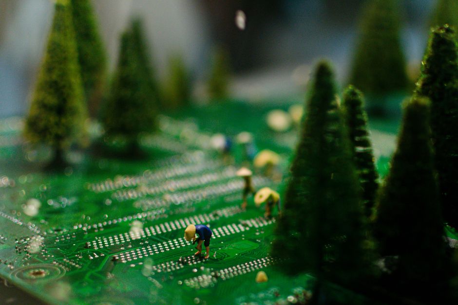 Creative scene of miniature figures farming on a circuit board with artificial trees.