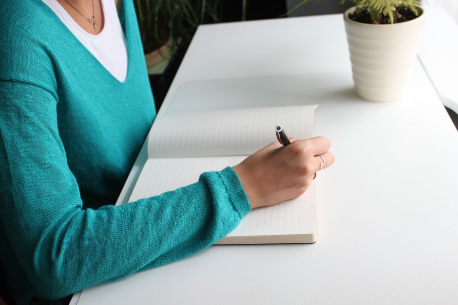 A woman writing in a notebook at a minimalist white desk indoors, emphasizing productivity.