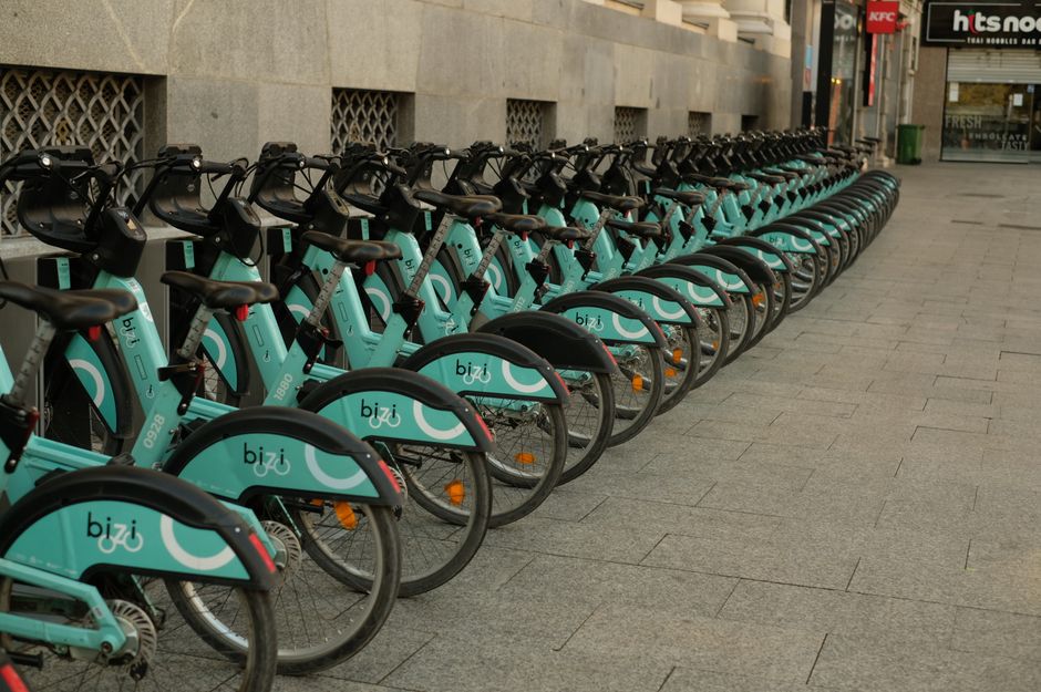 A line of turquoise electric rental bikes parked in a city, promoting eco-friendly transportation.