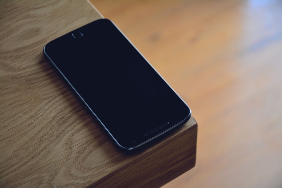 A smartphone sits quietly on the edge of a wooden table, displaying modern technology's sleek design.